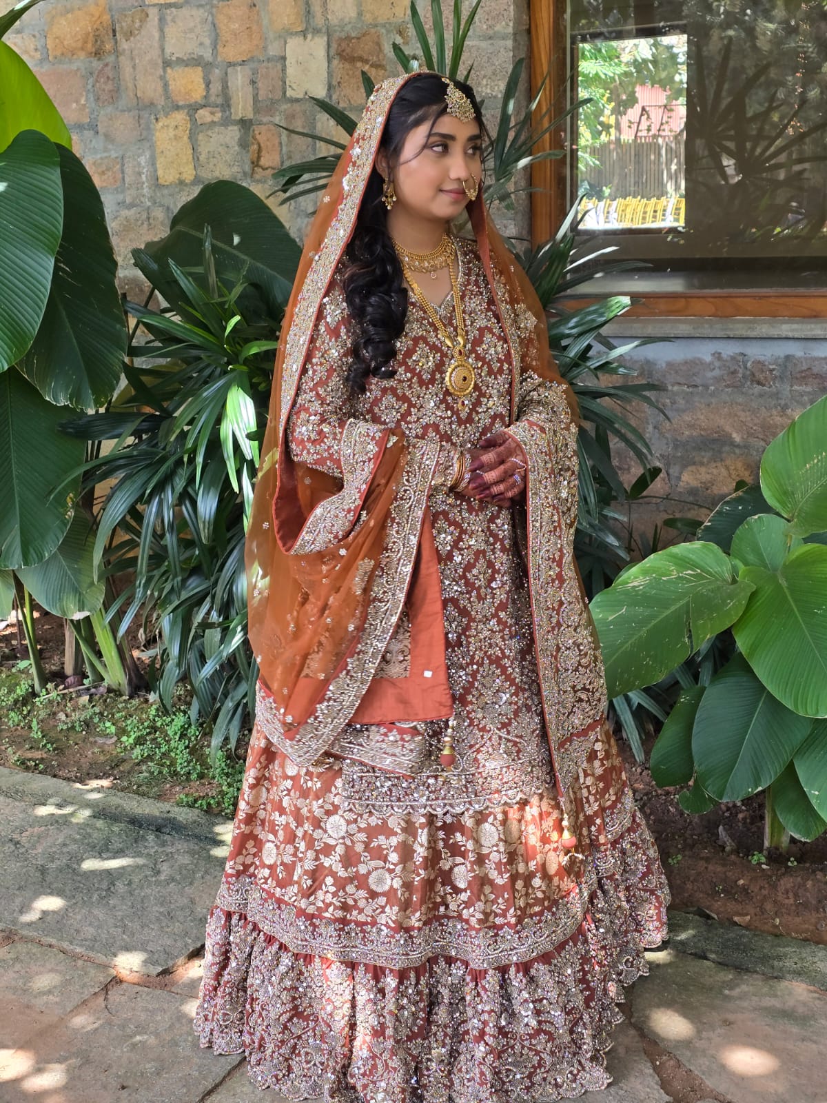 Bride in red rust traditional lehenga with gold embroidery standing outdoors